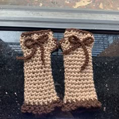 two crocheted mittens with brown bows are sitting on a window sill