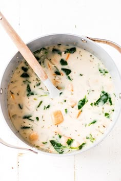 a pot filled with broccoli and cheese on top of a white table next to a wooden spoon