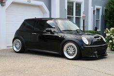 a small black car parked in front of a house next to a flower pot and bushes