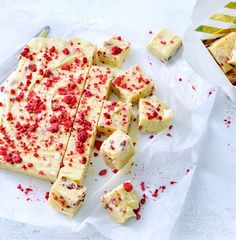 pieces of cake sitting on top of white paper next to a knife and bowl with red sprinkles