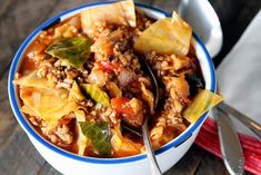 a bowl filled with meat and vegetable soup next to a spoon on a wooden table