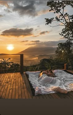 a woman laying on top of a bed next to a wooden deck under a cloudy sky