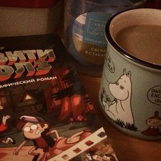 a coffee cup sitting next to a book on top of a wooden table with other books