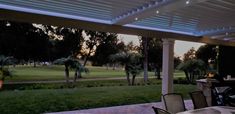 an outdoor dining area with tables and chairs under a pergolated roof at dusk