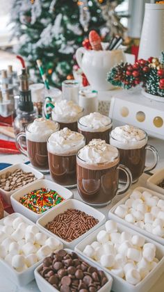 hot chocolates and marshmallows are on display in front of a christmas tree