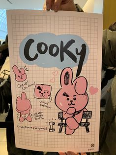 a person holding up a sign that says cooky with some drawings on the front