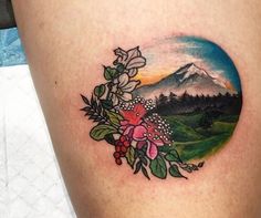 a woman's thigh with flowers and mountains in the background