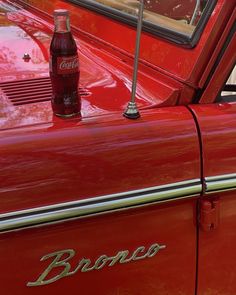 an old red car with a coke bottle sitting on the hood and window sill