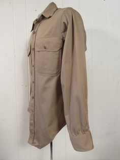 "Vintage 1940s or 50s khaki cotton work shirt. Has two button down pockets, button front and button cuffs. Made in Dayton Ohio by Lion Built Uniforms. Fits like a medium. Actual measurements are: 42\" at the chest 40\" at the waist Shoulder seam to shoulder seam: 16\" Shoulder seam to cuff: 23.5\" Overall length: 30\" In very good condition." Khaki Collared Utility Shirt, Khaki Collared Shirt With Snap Buttons, Vintage Beige Cotton Shirt, Vintage Brown Shirt For Workwear, Vintage Beige Shirt With Pockets, Vintage Shirt With Spread Collar For Work, Vintage Beige Shirt With Button Closure, Vintage Shirt With Button Closure For Work, Vintage Workwear Shirt With Pockets