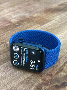 an apple watch on a wooden table with a blue band and the time displayed below it