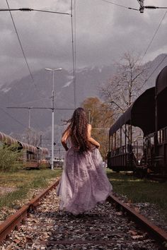 a woman in a long dress is walking down the railroad tracks near a train car