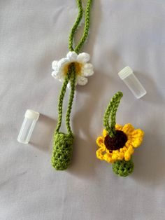 two crocheted flowers are attached to plastic tubes on a white sheet with one flower in the middle