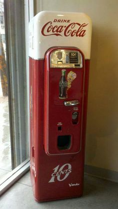 an old fashioned coca - cola machine sitting in front of a window with the door open