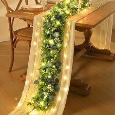 the table is decorated with green garland and fairy lights on it, along with greenery