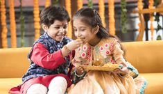 two children sitting on a yellow couch eating food from a plate in front of them