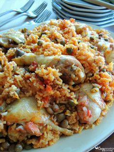 a white plate topped with rice covered in meat and veggies next to silverware