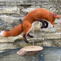 a red fox is jumping over a small wooden object on a glass table in front of a stone wall