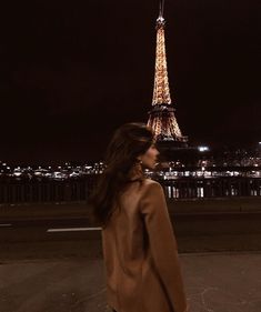 a woman standing in front of the eiffel tower at night with her back to the camera