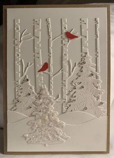 a white card with red birds sitting on top of trees and snow covered ground in the background