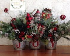 three metal buckets filled with pine cones and plaid christmas decorations on top of a wooden table