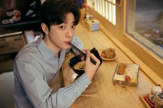 a young man sitting at a table eating food with chopsticks in his mouth