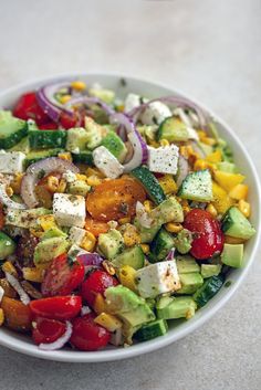 a salad with tomatoes, cucumbers, onions, corn and feta cheese