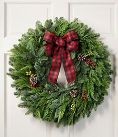 a christmas wreath hanging on the front door with pine cones, evergreens and red plaid bow