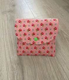 a pink flowered envelope sitting on top of a wooden floor next to a green button