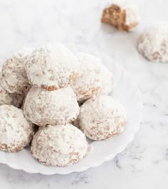 a plate full of powdered sugar cookies on a marble counter top with one cookie in the foreground