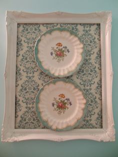 two plates with flowers on them are sitting in a white frame against a blue wall