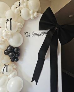 the balloon arch is decorated with black and white balloons, tied with a black ribbon