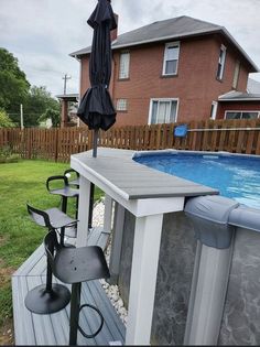 an umbrella and some chairs on a deck near a pool with a hot tub in the background