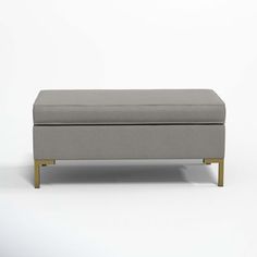 a grey ottoman with wooden legs and a white background