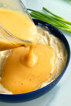 a blue bowl filled with mashed potatoes and gravy being drizzled over