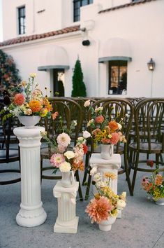 several vases with flowers are lined up on the ground in front of rows of chairs