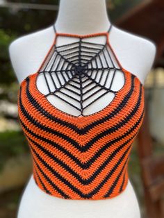 a white mannequin with an orange and black knitted spider web top on it