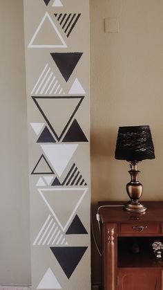 a lamp sitting on top of a wooden table next to a wall with black and white designs