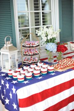 an american flag table with cupcakes, cookies and flowers in front of a window