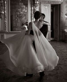 a woman in a black and white photo is holding her dress while walking through an ornate room