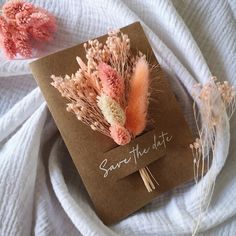 two dried flowers on top of a brown card with save the date written on it