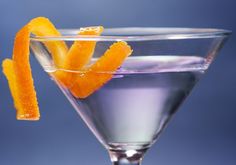 an orange peel garnishes the rim of a martini glass filled with pink liquid