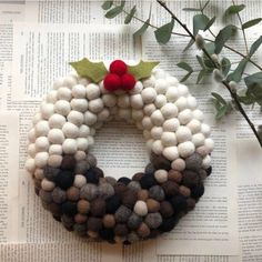 a christmas wreath made out of wool balls and felt with a red berry on top