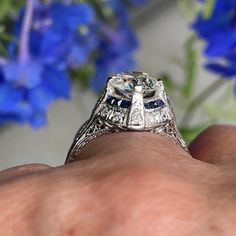 a close up of a person's hand holding a diamond and sapphire engagement ring