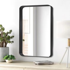 a mirror sitting on top of a wooden dresser next to a lamp and potted plant