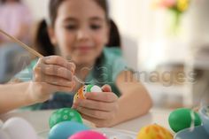 two girls painting easter eggs on a table with other children in the background and one girl holding a paintbrush