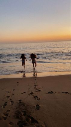 two people are walking on the beach with their feet in the water and footprints in the sand