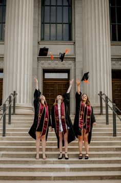 three women in graduation gowns standing on steps with their arms in the air and throwing caps into the air