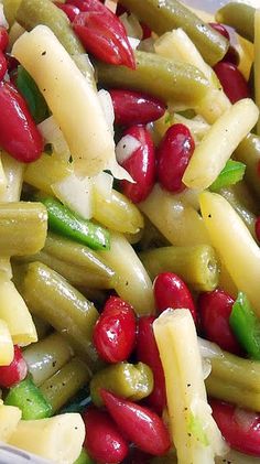 a white bowl filled with green beans, red peppers and other food items on top of it