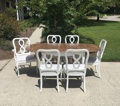 a wooden table with white chairs around it in the middle of a sidewalk near some trees