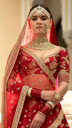 a woman in a red and gold bridal gown with jewelry on her head, wearing a